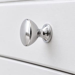 May include: A polished chrome cabinet knob with a smooth, rounded, mushroom-shaped head and a tapered base. The hardware features a highly reflective, mirror-like metallic finish and is mounted onto a flat, white, horizontal panelled surface.