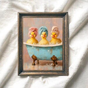Può includere: Una stampa artistica incorniciata che raffigura tre anatroccoli gialli seduti in una vasca da bagno azzurra con piedini. Ogni anatroccolo indossa un piccolo asciugamano avvolto intorno alla testa come un turbante. La vasca è piena di bolle.