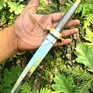 May include: A double-edged dagger featuring a polished steel blade, a ribbed metallic handle, and a brass crossguard. The knife has a pointed tip and a symmetrical design, with the metallic surfaces reflecting light against the sharp, tapered edges.