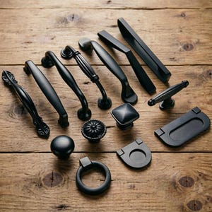 Puede incluir: Una colección de herrajes para armarios en negro mate que incluye varios tiradores de cajón, pomos y tiradores abatibles. El surtido presenta barras curvas lisas, diseños estriados, un pomo cuadrado, un pomo redondo y un tirador de anilla.