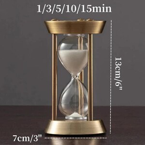 Pu&ograve; includere: Una clessidra con cornice in ottone spazzolato e bulbi in vetro trasparente contenenti sabbia bianca. Il testo 1/3/5/10/15min &egrave; visibile in alto. Le dimensioni indicate sono 13 cm di altezza e 7 cm di larghezza sulla cornice.