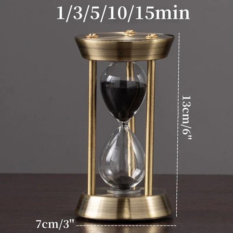 Pu&ograve; includere: Una clessidra con cornice in ottone spazzolato e sabbia nera. Il testo 1/3/5/10/15min &egrave; visibile sopra. Le dimensioni indicate sono 13 cm di altezza e 7 cm di larghezza, mostrando la struttura in vetro e la base in metallo.