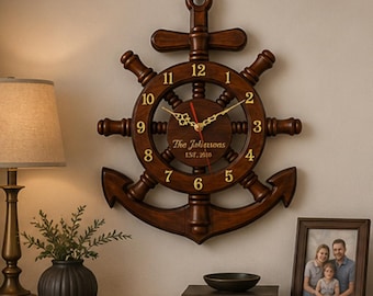 Può includere: Un orologio da parete in legno a forma di ancora con un design a ruota di nave. Il quadrante mostra l'ora con lancette e numeri dorati. Il testo "The Johnsons EST. 2010" è inciso sul quadrante.