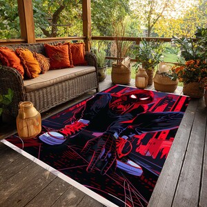 May include: A rectangular rug featuring a graphic of a superhero in a dynamic pose, set against a cityscape backdrop. The design incorporates bold red and black colors, with the superhero's suit and the city lights prominently displayed. The rug is placed on a wooden deck.