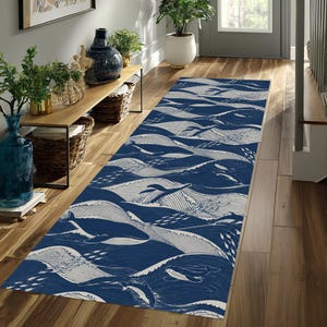 May include: A long rectangular runner rug featuring a repeating pattern of dark blue whales and white stylized ocean waves. The design includes small schools of fish swimming alongside the whales, creating a continuous nautical theme across the surface.
