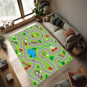 May include: A rectangular area rug featuring a vibrant green landscape with a winding gray road network, small red buildings, a blue pond, green trees, gray mountain peaks, and checkered finish line flags printed across the surface.