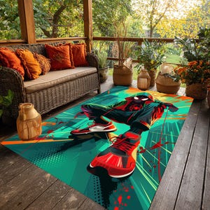 May include: A rectangular outdoor rug featuring a vibrant illustration of a superhero in a dynamic pose. The rug showcases a teal and green background with red and orange accents. The superhero is depicted in a red and black suit with red sneakers.