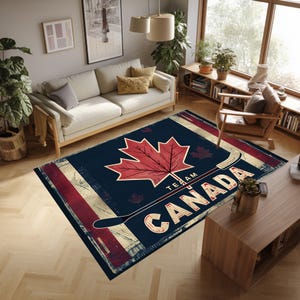 Peut inclure: Tapis rectangulaire avec un fond bleu marine, représentant une grande feuille d'érable rouge et les mots "TEAM CANADA" en blanc. Un graphisme de crosse de hockey est également présent. Le tapis a un aspect vieilli.