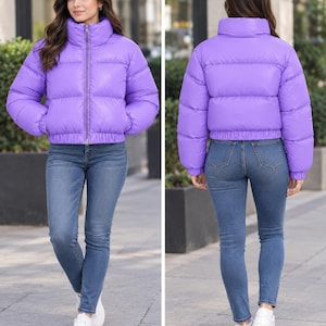 May include: A bright purple puffer jacket featuring a high collar, a full-length front zipper, long sleeves with elasticized cuffs, and a cropped hemline. The jacket is paired with blue denim jeans and white sneakers.