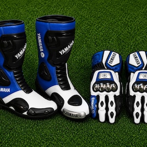 Puede incluir: Un par de botas de moto azules, blancas y negras junto a un par de guantes a juego. Las botas llevan el logotipo de Yamaha en el lateral y en la puntera. Los guantes cuentan con protectores metálicos en los nudillos y el logo de Yamaha.