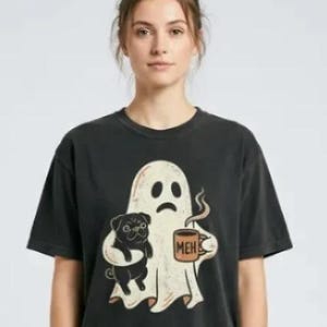 May include: A charcoal gray short-sleeve t-shirt featuring a graphic of a white ghost with a sad expression. The ghost is holding a black pug in one arm and a brown coffee mug with the text MEH printed on it in the other hand.