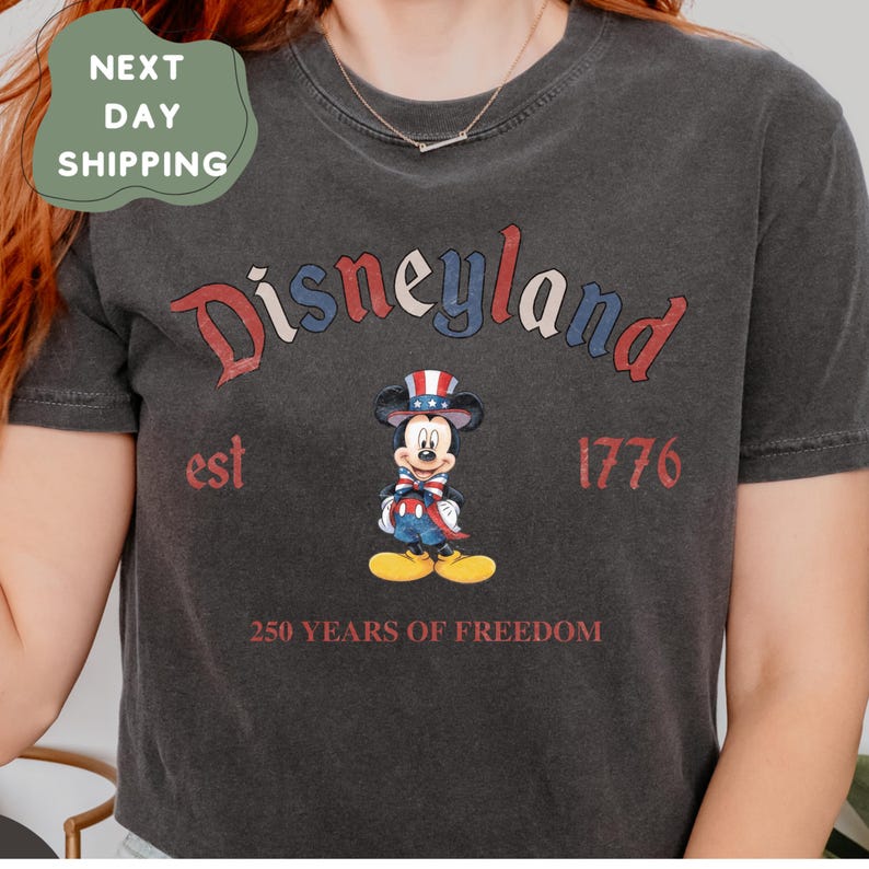 A person wearing a black t-shirt with a graphic design featuring Mickey Mouse and the text "Disneyland est 1776 250 YEARS OF FREEDOM".