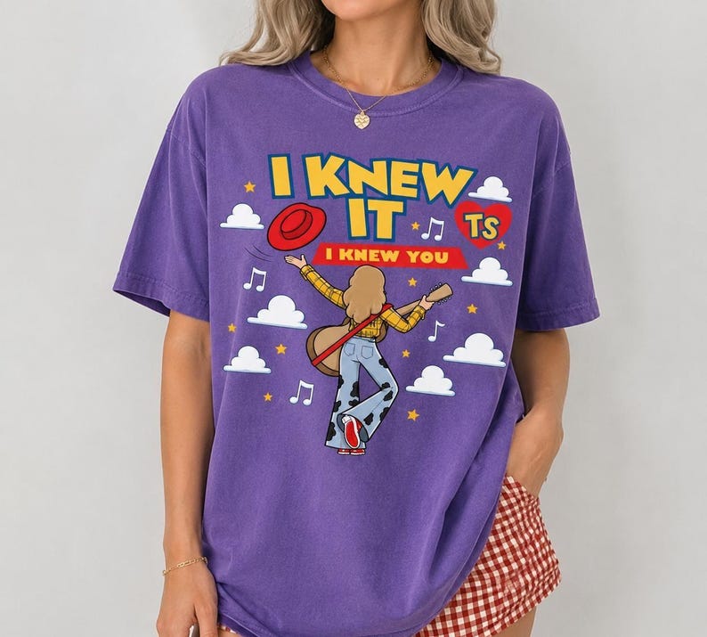May include: A purple short-sleeve t-shirt featuring a graphic of a person with blonde hair playing a guitar, wearing a yellow plaid shirt and cow-print bell-bottom pants. The text reads I KNEW IT and I KNEW YOU, surrounded by clouds and stars.