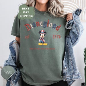 A person wearing a green t-shirt with a graphic of Mickey Mouse and text that says "Disneyland est 1776 250 years of freedom".