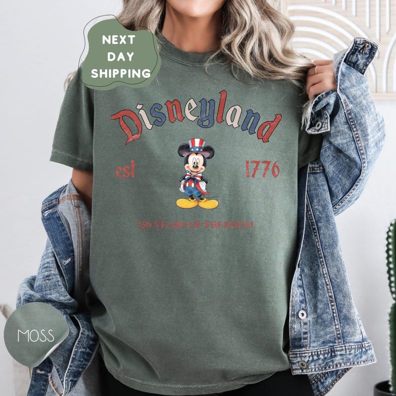 A person wearing a green t-shirt with a graphic of Mickey Mouse and text that says "Disneyland est 1776 250 years of freedom".