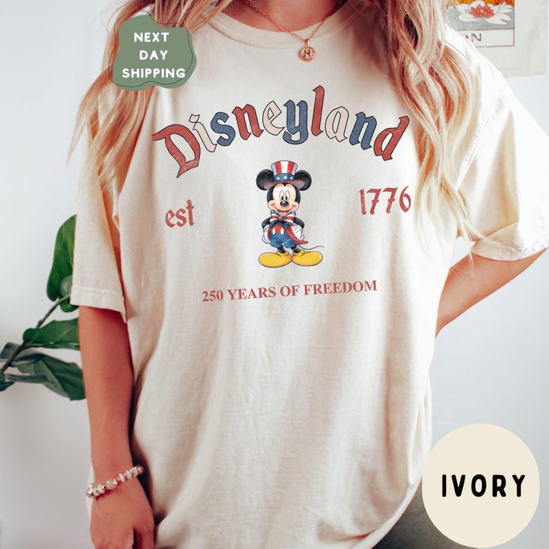 A person wearing a white t-shirt with the text "Disneyland est 1776 250 YEARS OF FREEDOM" printed on it, along with a Mickey Mouse graphic.