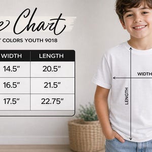 A young boy is standing in front of a size chart for a white t-shirt, smiling and posing for the camera.