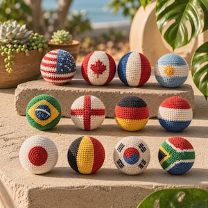 Puede incluir: Colección de bolas de ganchillo, cada una con el diseño de una bandera nacional. Las banderas incluyen EE. UU., Canadá, Francia, Argentina, Brasil, Inglaterra, Alemania, Países Bajos, Japón, Bélgica, Corea del Sur y Sudáfrica. Las bolas se muestran sobre una superficie de piedra.