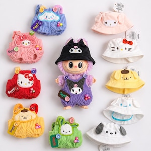 Op de afbeelding: Een verzameling Sanrio-thema pluche speelgoed en vissershoeden. Het pluche speelgoed heeft de vorm van overalls, met personages als Hello Kitty, Cinnamoroll en Pompompurin. De hoeden zijn in verschillende kleuren en hebben karakterontwerpen.