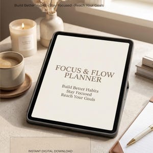 May include: A tablet displaying the text FOCUS & FLOW PLANNER, Build Better Habits, Stay Focused, Reach Your Goals on a light screen. The device is positioned on a surface with a candle, a ceramic mug, a notebook, and a pen nearby.