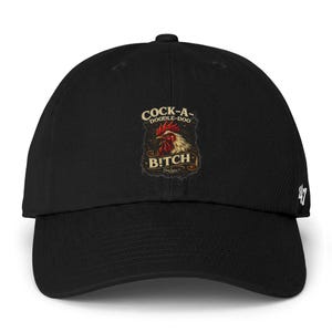 Può includere: Cappellino da baseball nero con visiera curva. Il cappellino presenta una grafica con il testo "COCK-A-DOODLE-DOO BITCH" e un'illustrazione di gallo in rosso, marrone e oro.