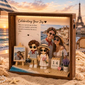 Könnte beinhalten: Ein hölzerner Schattenkasten mit einem Foto eines Paares in Paris, zwei aus Bausteinen gefertigten Figuren, einer Miniatur-Staffelei mit Foto und einem Kalenderblock mit der Zahl 14. Der Text lautet Celebrating Your Joy und eine Botschaft.