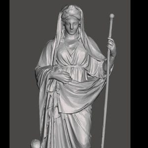 May include: A gray statue of a robed figure holding a staff. The figure has a draped head covering and stands on a rectangular base. A small pillar is visible to the left of the figure.