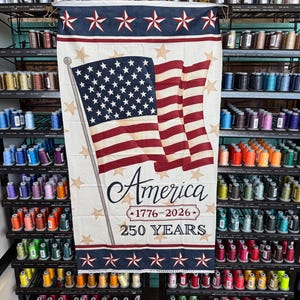May include: A vertical fabric banner featuring a waving American flag, the text America, 1776-2026, and 250 YEARS. The design includes a cream background with scattered tan stars, bordered by dark blue stripes with white stars at the top and bottom.