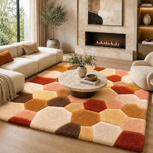 May include: A plush area rug featuring a repeating geometric honeycomb pattern in a warm colour palette of cream, beige, burnt orange, and deep brown. The rug has a thick, textured pile and covers a large portion of the floor space in the room.
