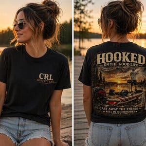 Puede incluir: Camiseta negra con "CRL OUTFITTERS" estampada en la parte delantera y una escena de pesca en la parte trasera con el texto "HOOKED ON THE GOOD LIFE". La camiseta se usa con pantalones cortos de mezclilla. El fondo muestra un lago al atardecer.