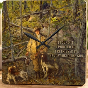 May include: A square wall clock featuring a printed painting of a hunter in a forest with two dogs and a bird. The text reads: I FOUND IT I POINTED IT I RETRIEVED IT HE JUST HELD THE GUN. The clock has black hands and a dark, earthy color palette.
