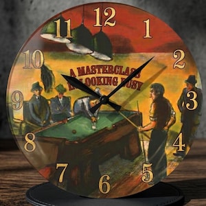 May include: A round wall clock featuring a printed illustration of people playing billiards. The scene includes a green pool table, hanging lamps, and the text A MASTERCLASS IN LOOKING BUSY. The clock has black hour, minute, and second hands with gold numbers.