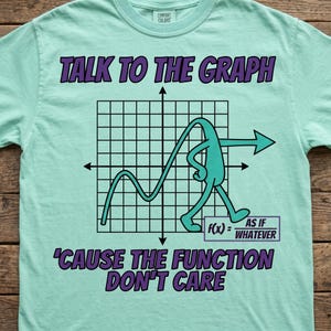 Puede incluir: Una camiseta de color verde menta claro con un gráfico de cuadrícula negra y un personaje de dibujos animados de color cerceta caminando sobre él. El texto dice TALK TO THE GRAPH, f(x) = AS IF WHATEVER y 'CAUSE THE FUNCTION DON'T CARE.