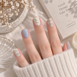 May include: Fingernails featuring a multi-design manicure with solid light blue, solid grey, white cable knit texture, and a light blue, white, and tan plaid pattern. The nails are short and rounded, showcasing a clean, polished aesthetic.
