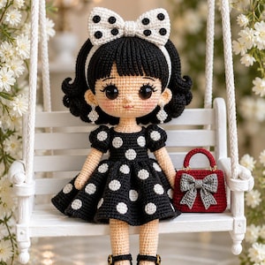 May include: A handmade crochet doll with black hair, a white bow with black polka dots, and a black dress with white polka dots. The doll is wearing black and white polka dot shoes and holding a red purse with a gray bow. The doll is sitting on a white swing.