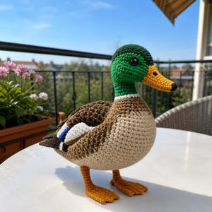 May include: A handmade crochet duck with a green head, brown and tan body, and orange feet and beak. The duck has a detailed design, with a white stripe on the wing. The duck is a decorative item.