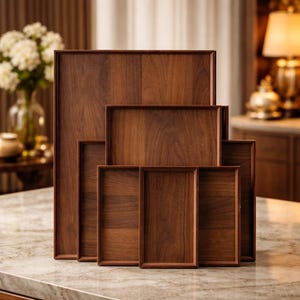 May include: A set of six wooden serving trays in different sizes. The trays are rectangular with a dark brown finish and a raised edge. The trays are arranged in a nested configuration, with the largest tray at the back and the smallest at the front.