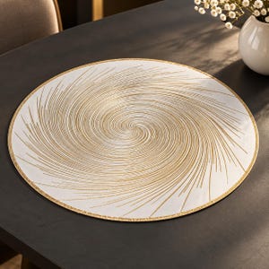Könnte beinhalten: Ein rundes, weißes Platzset mit einem metallisch goldenen Spiralmuster, das von der Mitte zu den Rändern ausstrahlt. Die kreisförmige Unterlage hat einen dünnen goldenen Rand und eine glatte Oberfläche, die einen Kontrast erzeugt.