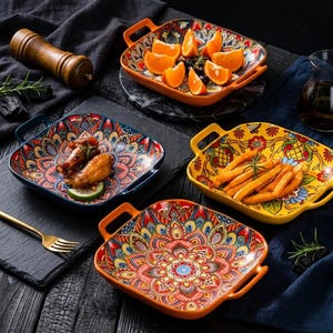 May include: A collection of colorful, square ceramic serving dishes with handles, featuring intricate floral and geometric patterns. Some dishes hold food, including orange slices and french fries. A wooden pepper grinder and a gold fork are also visible.