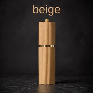 May include: A beige, ribbed wooden pepper mill with brass accents. The mill is cylindrical with a gold-colored top and a band of gold around the middle. The word "beige" is displayed in the upper left corner.