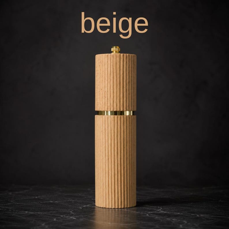 May include: A beige, ribbed wooden pepper mill with brass accents. The mill is cylindrical with a gold-colored top and a band of gold around the middle. The word "beige" is displayed in the upper left corner.