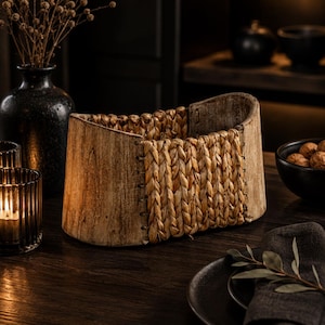 Op de afbeelding: Een houten mand met een geweven middenstuk. De mand heeft een lichtbruine kleur met een natuurlijke houtnerf. Het geweven gedeelte is gemaakt van lichtbruin materiaal. De mand staat op een donkere houten tafel.