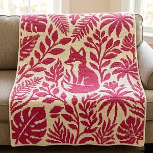 May include: A rectangular crochet blanket featuring a repeating pattern of dark pink botanical leaves and ferns on a cream background, with a central graphic of a sitting fox rendered in the same dark pink and cream color scheme.