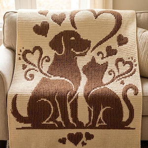 Peut inclure: Une couverture en crochet de couleur crème présentant un motif marron foncé représentant un chien et un chat assis côte à côte. Le design comprend plusieurs formes de cœurs entourant les animaux, avec un grand cœur au-dessus des figures.