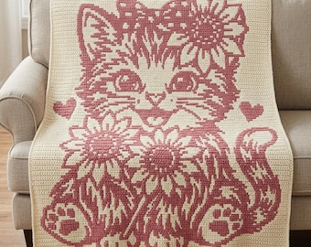 May include: A cream-colored crochet blanket featuring a large, dark pink graphic of a kitten with a sunflower on its head, two sunflowers at its feet, and two small hearts on either side. The design is created with a dense, uniform stitch pattern.