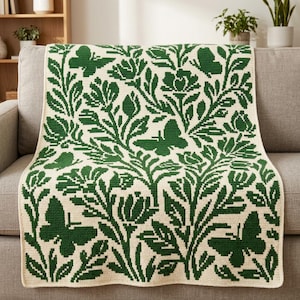 May include: A rectangular crochet blanket featuring a repeating pattern of dark green butterflies, flowers, and leafy vines set against a cream-colored background. The textile displays a dense, textured stitch construction with a symmetrical botanical design.