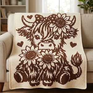May include: A cream-colored crochet blanket featuring a dark brown graphic pattern of a Highland cow. The cow is adorned with a sunflower on its head and is holding two large sunflowers, surrounded by three small heart shapes in the design.