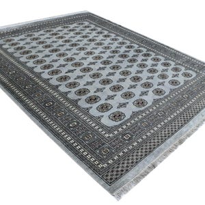 Peut inclure: Un tapis rectangulaire bleu clair avec un motif complexe. Le tapis présente un motif répétitif de formes ovales avec un motif central, encadré par une bordure détaillée dans des tons de gris et de marron. Le tapis a une frange sur les bords.