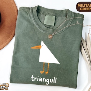 May include: A military green t-shirt featuring a white triangular seagull graphic with an orange beak and striped orange legs. Below the graphic, the word "triangull" is printed in white. A small gold-toned necklace rests on the neckline.