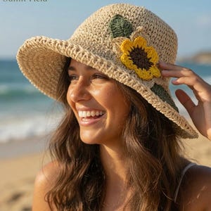 May include: A beige crochet sun hat featuring a large yellow sunflower applique with a dark brown center and two dark green leaves attached to the side. The hat has a wide, flexible brim and a textured, woven construction throughout the crown.